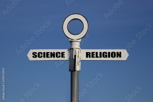 Old road sign with science and religion pointing in opposite directions against a blue sky