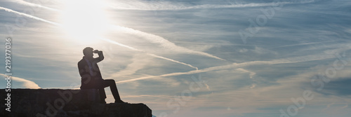 Wide panorama view of businessman in a suit sitting on a wall