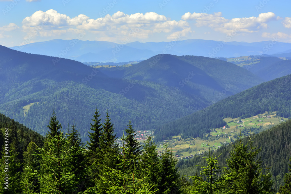 landscapes of mountains covered with dense coniferous forest, against a blue sky with clouds