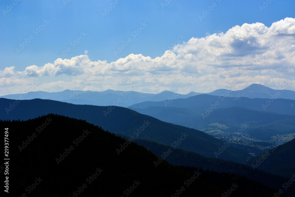 Obraz premium landscapes of mountains covered with dense coniferous forest, against a blue sky with clouds