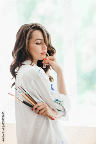 Beautiful thoughtful woman artist with brushes posing in her studio