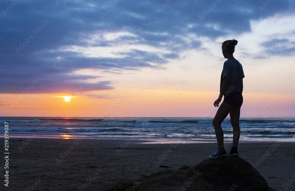 Girl on the beach at sunset with sun over the sea, city of San Sebastian