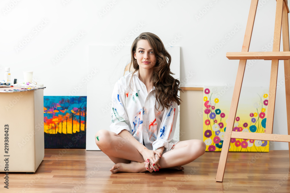 Pretty woman painter sitting on the floor in front of canvas and drawing Pretty woman painter sitting on the floor in front of canvas and drawing