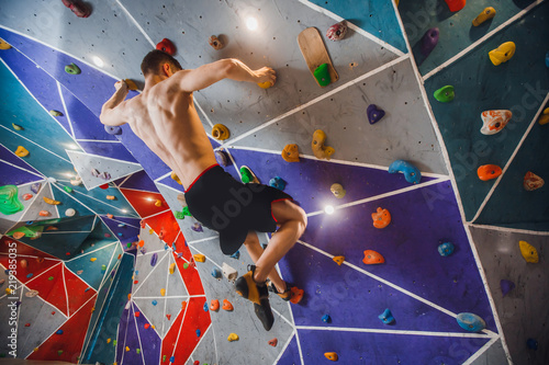 Close-up of male climber on sport climbing gym wall holding onto ledges.