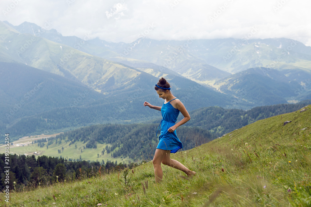 girl in blue long dress standing on a high mountain in a meadow on a background of sheep