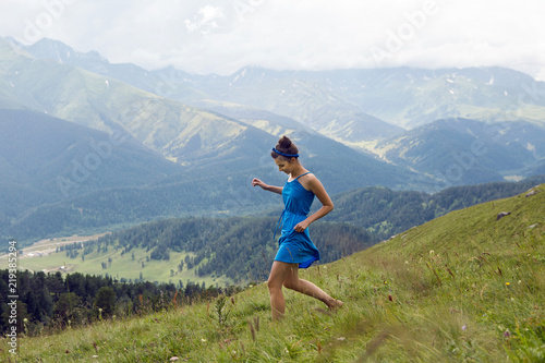 girl in blue long dress standing on a high mountain in a meadow on a background of sheep