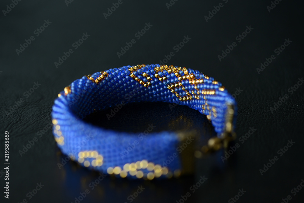 Blue beaded bracelet with golden pattern on a dark background close up Blue beaded bracelet with golden pattern on a dark background close up