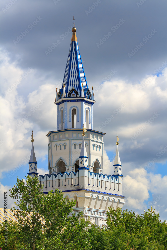 Watchtower of Izmailovo Kremlin on a background of green trees and cloudy blue sky in Moscow