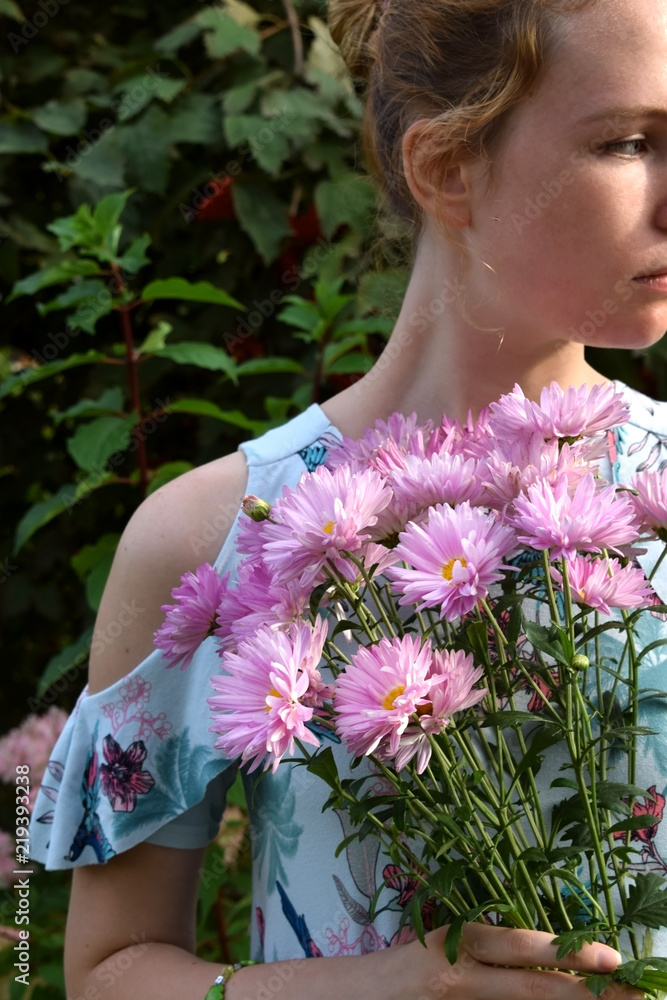 Naklejka premium Young woman is holding pink chrysanthemum flowers on a sunny day in the park