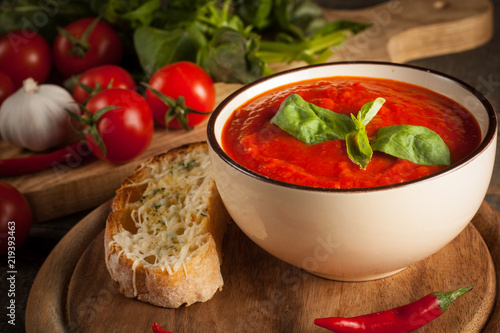 Fresh, healthy tomato soup with basil, pepper, garlic, tomatoes and bread on wooden background. Spanish gazpacho soup.