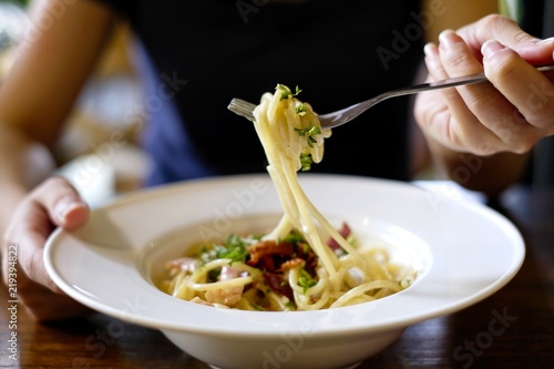 Italian cuisine, A female hand is trying to use fork to eat Spaghetti Cabana or Spaghetti White Sauce on white dish at restaurant