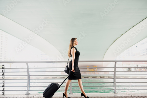 Young modern confident business woman pulling a suitcase in a Dubai Marine. Starting a new job in a big city.