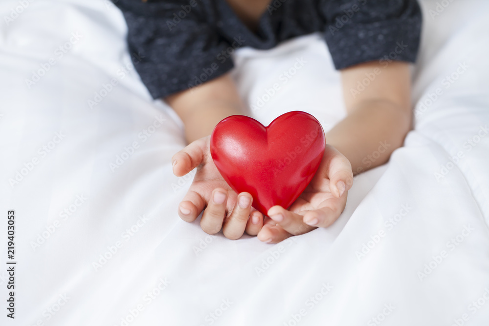 child holding red heart in his hands, offering love on the bedroom. child holding red heart in his hands, offering love on the bedroom.