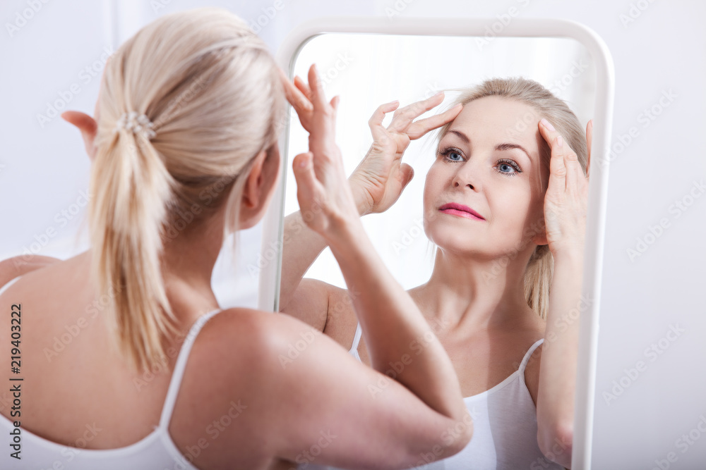 Middle aged woman looking at wrinkles in mirror. Plastic surgery and collagen injections. Makeup. Macro face. Selective focus Middle aged woman looking at wrinkles in mirror. Plastic surgery and collagen injections. Makeup. Macro face. Selective focus