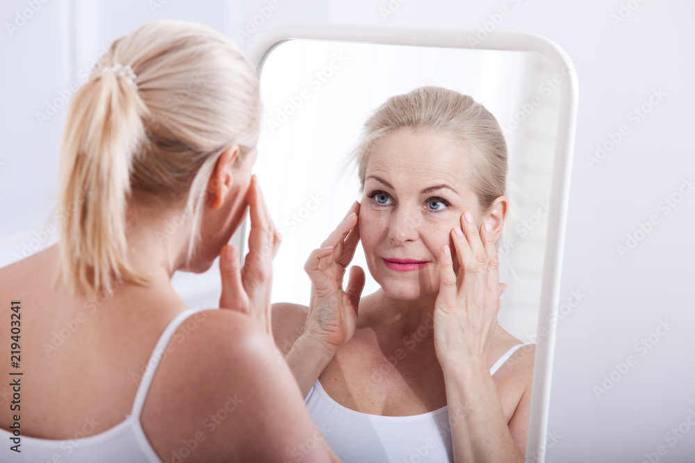 Middle aged woman looking at wrinkles in mirror. Plastic surgery and collagen injections. Makeup. Macro face. Selective focus