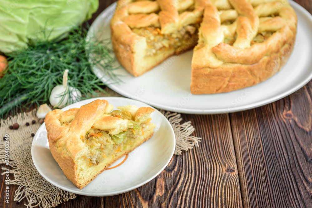 Homemade pie with cabbage, carrot, onion and meat on wooden background.