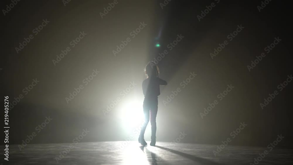 Child is dancing energetic movements in the studio. Black smoke background. Silhouette. Light from behind Child is dancing energetic movements in the studio. Black smoke background. Silhouette. Light from behind