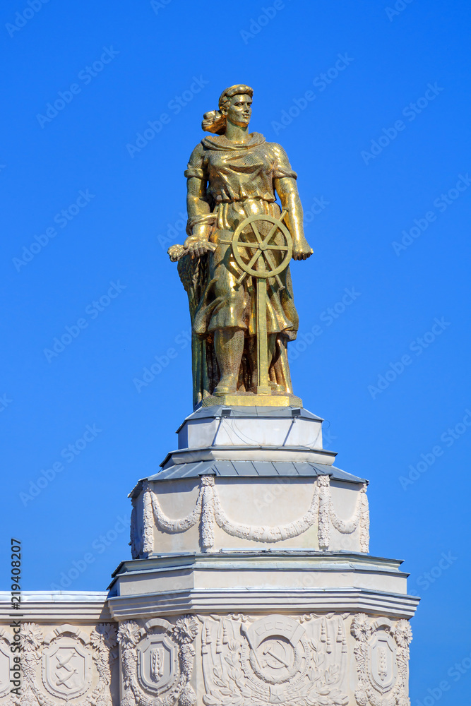 Figure of a woman of tractor driver on a roof of pavilion Space on Exhibition of Achievements of National Economy (VDNH) in Moscow against blue sky