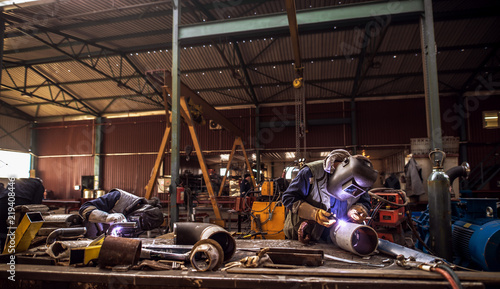 Front view of a industry work space with people in protective uniform cutting metal pipes.
