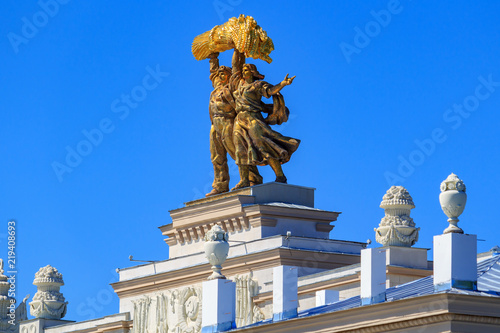 Gilded figures of Tractor driver and collective farm girl on top of arch of Main entrance on VDNH in Moscow closeup on a sunny summer morning against blue sky
