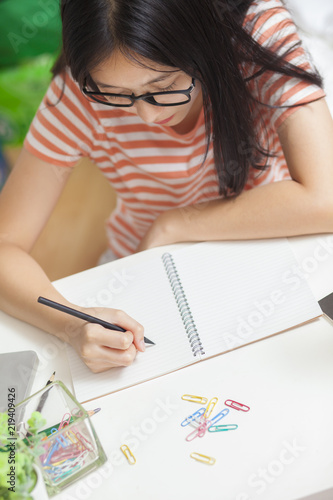 Asian adorable girl be happy and smiling writing note book with use laptop computer to work at home.Girl sitdown at living room.working online lifestyle top view.