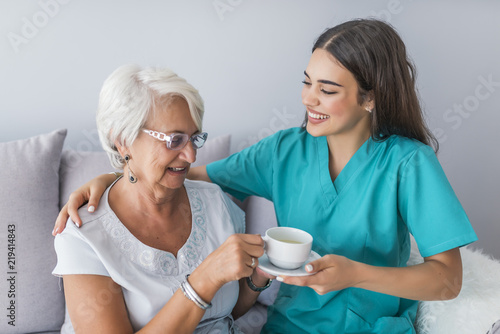 Young caregiver in uniform hugging smiling elderly woman during a home visit