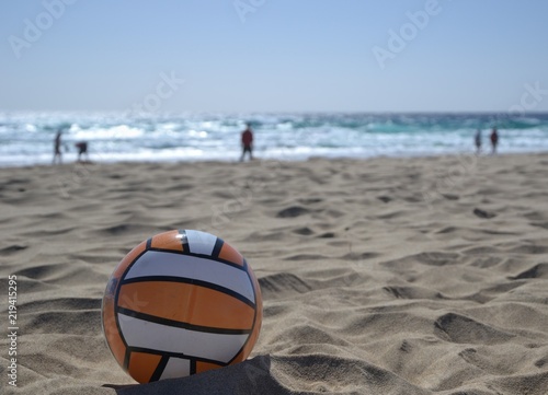 Beach ball on the sandy beach. Blurred background with ocean and people silhouettes