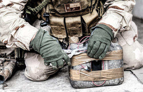 Army soldier, anti terrorist team combat engineer, ammunition technical officer, explosives military expert using pliers to cut wire on improvised explosive device, neutralizing homemade bomb on floor