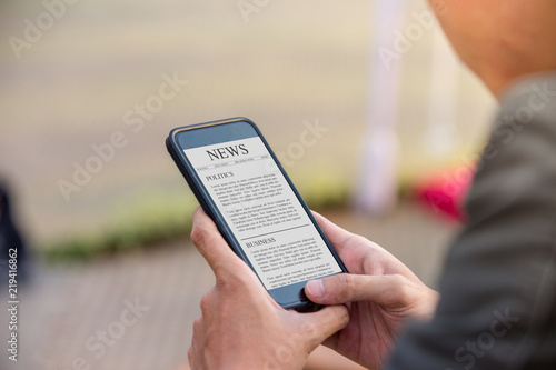 News article concept on phone screen. Man holding smartphone reading news article on screen.