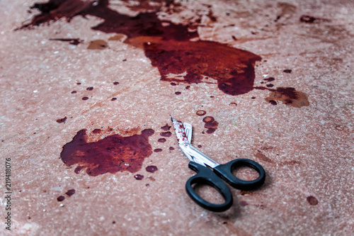 Trauma shears or bandage scissors lying on floor with stains of human blood around. Blood loss and bleeding stop, emergency medical aid for gunshot wounds, tactical combat casualty care on battlefield photo