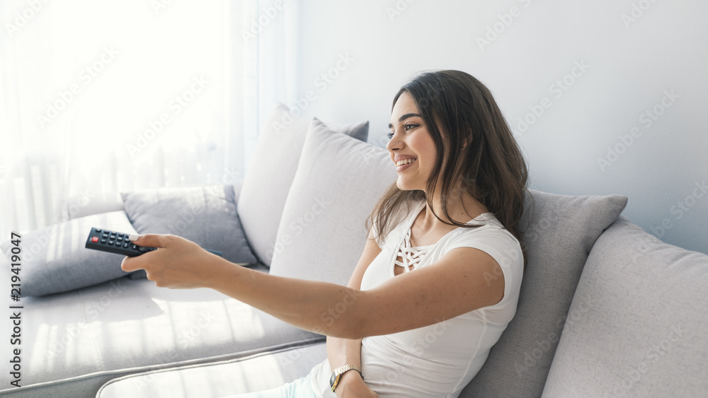 Relaxed young brunette woman lying on sofa and watching tv Relaxed young brunette woman lying on sofa and watching tv