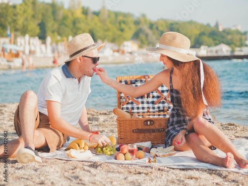 Young couple spending time on date together on the beach. Boyfriend and girlfriend on picnic. They relaxing, feeds, love each other. Relationship concept.