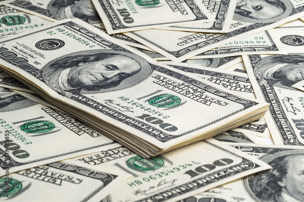 A pack of one hundred dollar bills in the background of scattered dollars. View at an angle A pack of one hundred dollar bills in the background of scattered dollars. View at an angle