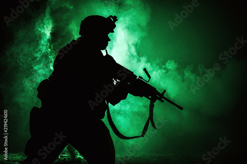 Silhouette of modern infantry soldier, elite army fighter in tactical ammunition and helmet, standing with assault service rifle in hands