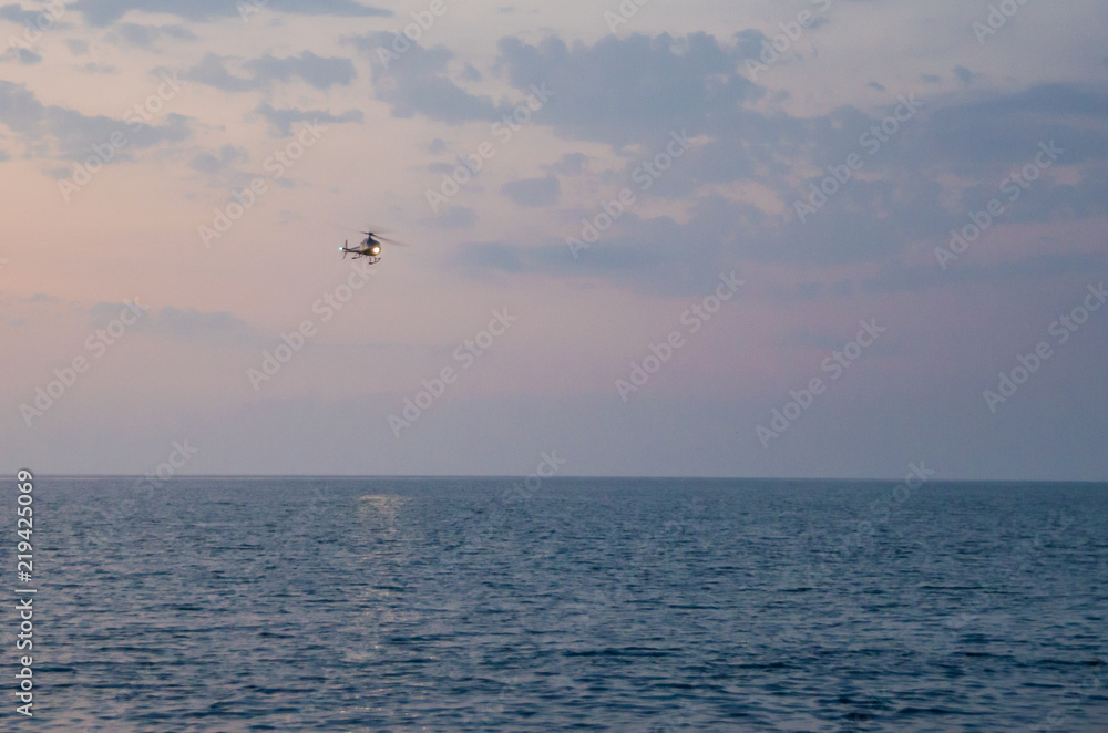 Silhouette of helicopter flying against amber sky during sunset over sea