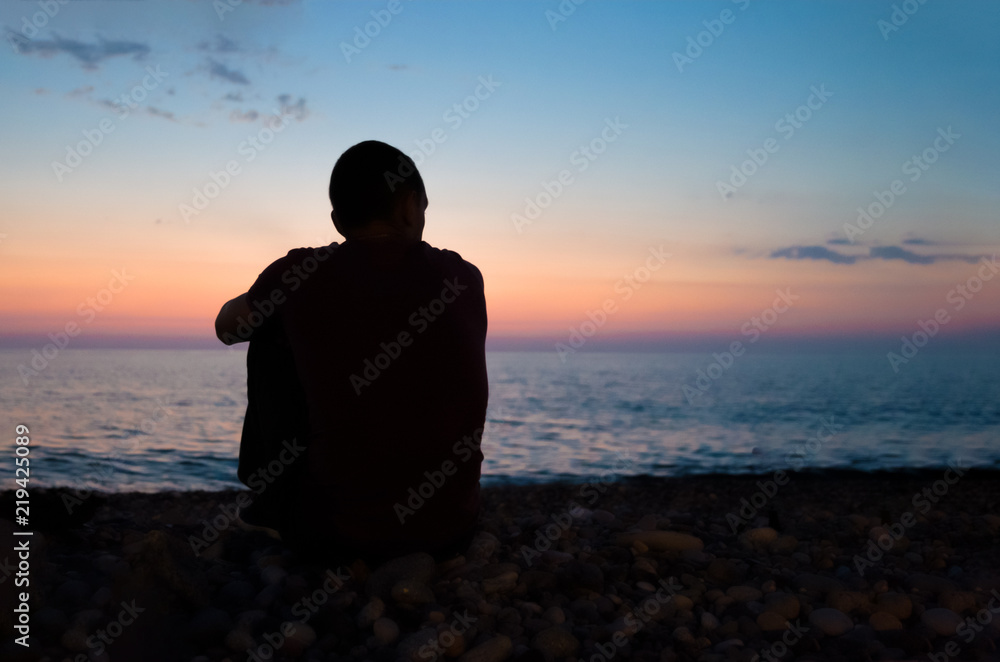 the man is sitting on the seashore and watching the sunset the man is sitting on the seashore and watching the sunset