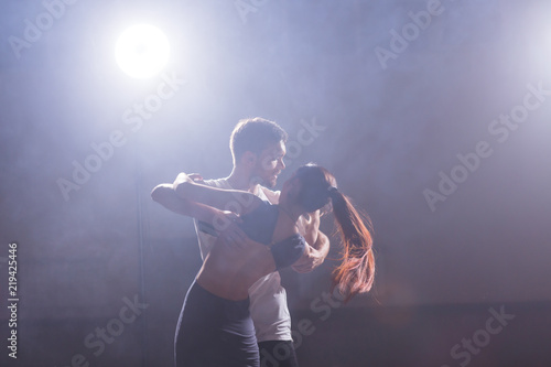 Skillful dancers performing in the dark room under the concert light and smoke. Sensual couple performing an artistic and emotional contemporary dance