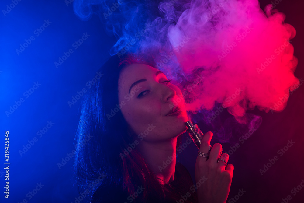 Fototapeta premium Portrait of asian woman smoking vape or e-cigarette in neon light at black background.