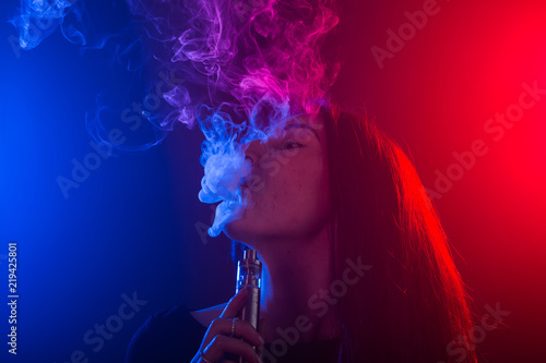 Portrait of girl in colored neon smoke with vape or electronic cigarette. photo