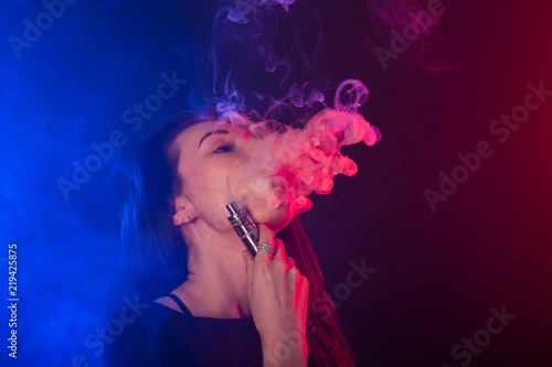 Portrait of young woman in neon red and blue smoke with vape or e-cigarettes.