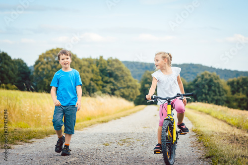 Junge und Mädchen laufen und fahren Fahrrad auf einem Feldweg