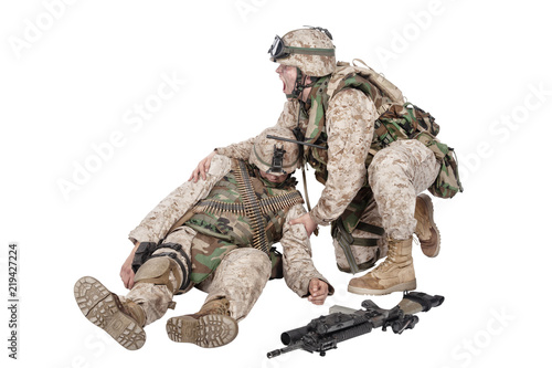 Fototapeta Military medic, commando shaking for shoulders, trying bring to consciousness, checking condition of unconscious, wounded soldier or comrade, isolated on white