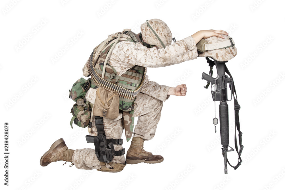 Army soldier in sorrow for fallen comrade, standing on knee, leaning on rifle with helmet and two dog tags on chain, studio shoot isolated on white. Military funeral honors, grief for killed in action Army soldier in sorrow for fallen comrade, standing on knee, leaning on rifle with helmet and two dog tags on chain, studio shoot isolated on white. Military funeral honors, grief for killed in action