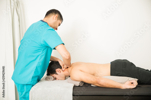 Doctor Giving Physical Therapy To Shirtless Athlete Lying In Bed