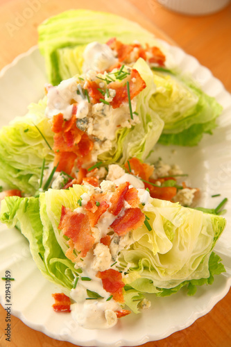 Vertical view of lettuce wedges topped with blue cheese dressing, bacon and chives