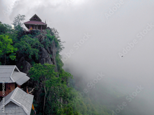 Wat Chaloem Phrakiat Phrachomklao Rachanuson at Chae hom, Lampang, Thailand. Buddhist temple and pagoda on rock mountain have clouds and fog. Bird are flying. photo