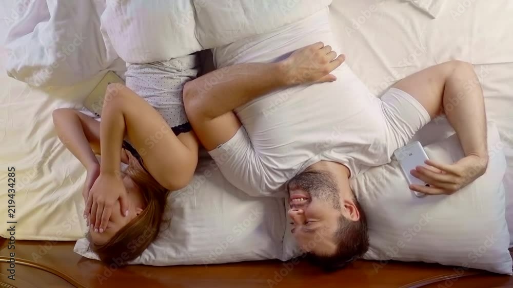 husband is making smile his young wife lying on a bed in morning time, woman is laughing and closing her face husband is making smile his young wife lying on a bed in morning time, woman is laughing and closing her face