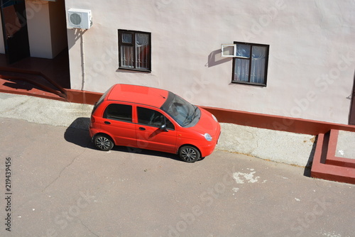 Red four-door car on against a pink building with bright sun rays
