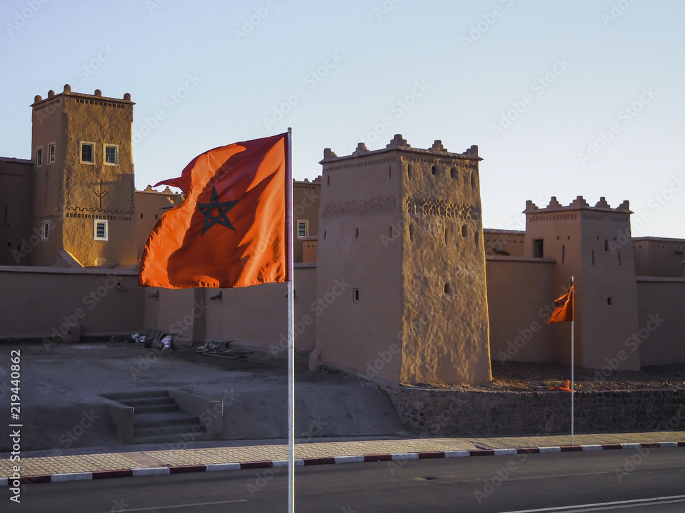 Moroccan flag flying with Ait Benhaddou in the background during sunset