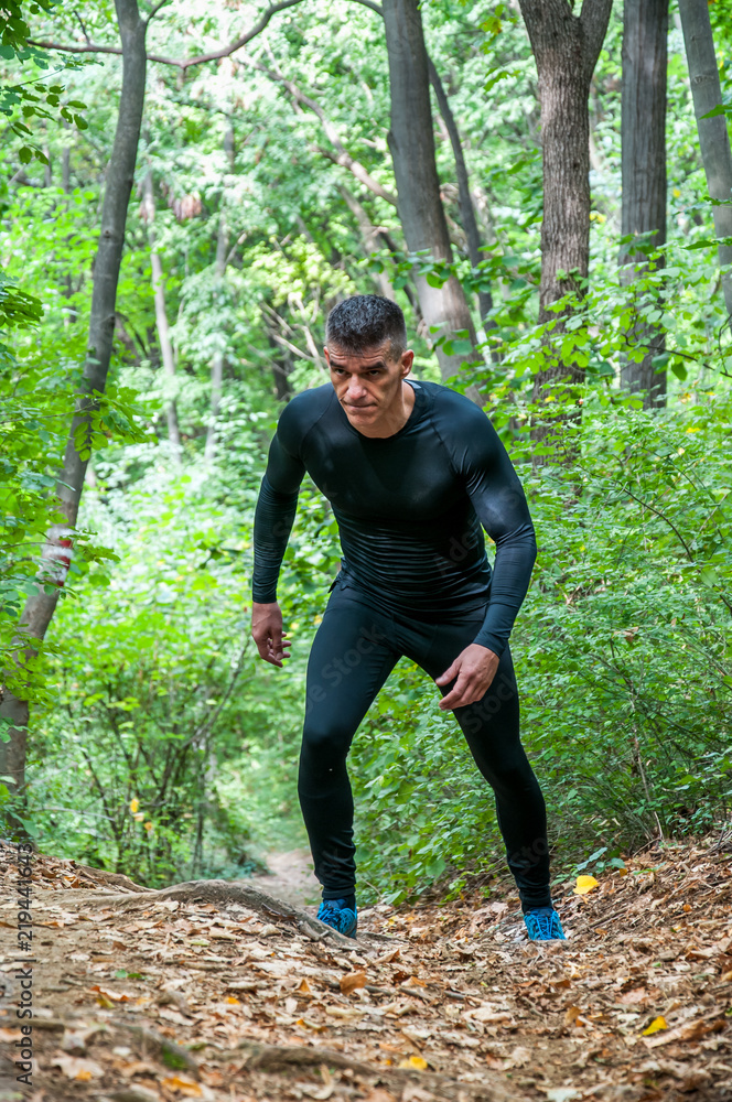 Young active muscular man in sportswear running through the footpath in nature in the forest for cardio workout vertical image Young active muscular man in sportswear running through the footpath in nature in the forest for cardio workout vertical image